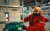 REWE employee in red uniform organizes delivery boxes in the warehouse for the REWE delivery service.