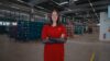 REWE employee in a red work outfit stands with her arms crossed in a warehouse.