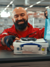Lächelnder REWE Mitarbeiter mit Scanner und REWE Tüte